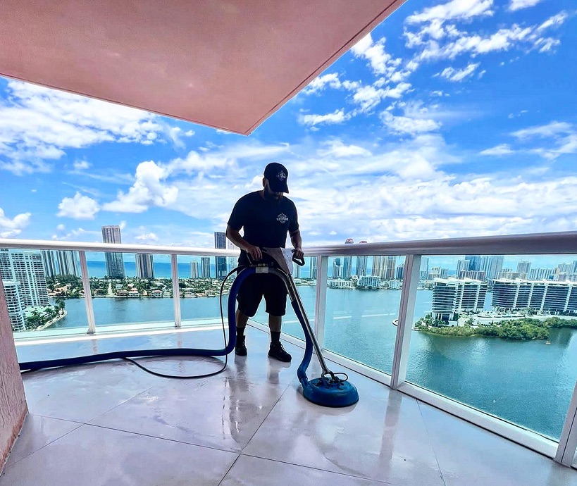 Tony of Extreme Steam cleaning a high-rise balcony with the Miami skyline behind him