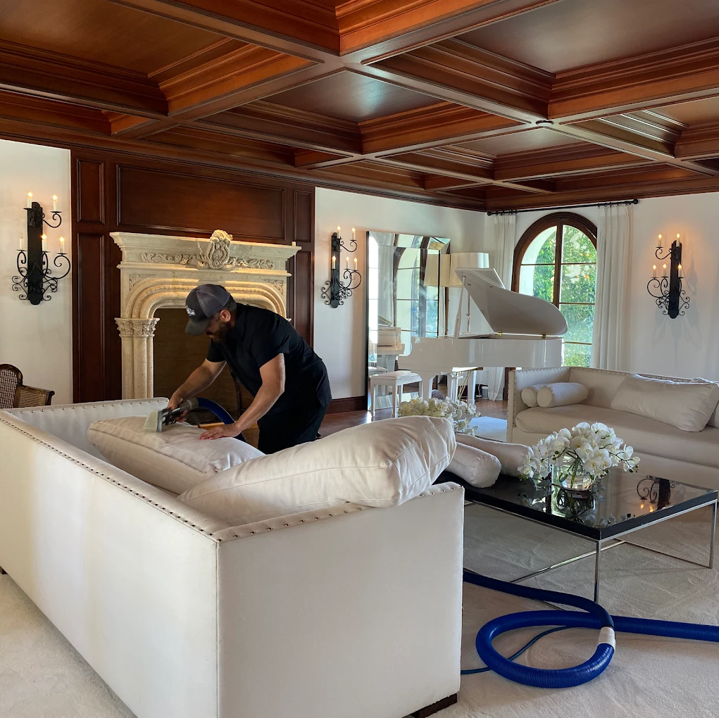 Technician steam cleaning a white sofa in a living room