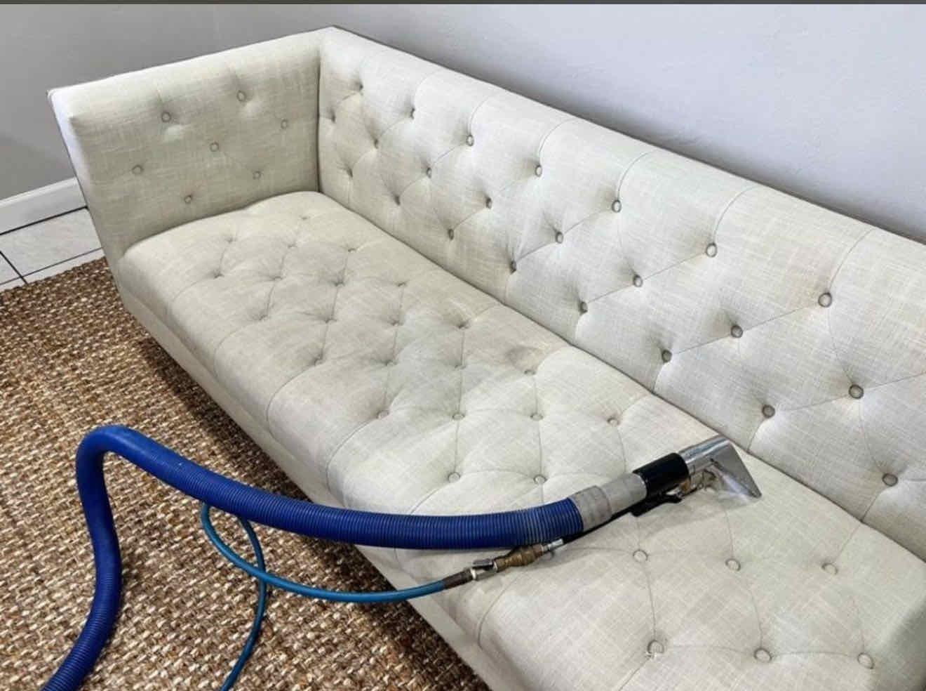 Steam wand deep-cleaning a white tufted sofa